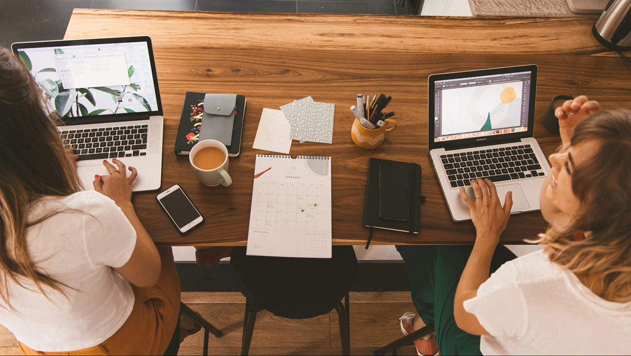 Photograph of two small business owners sitting at their kitchen table while working at their laptops.