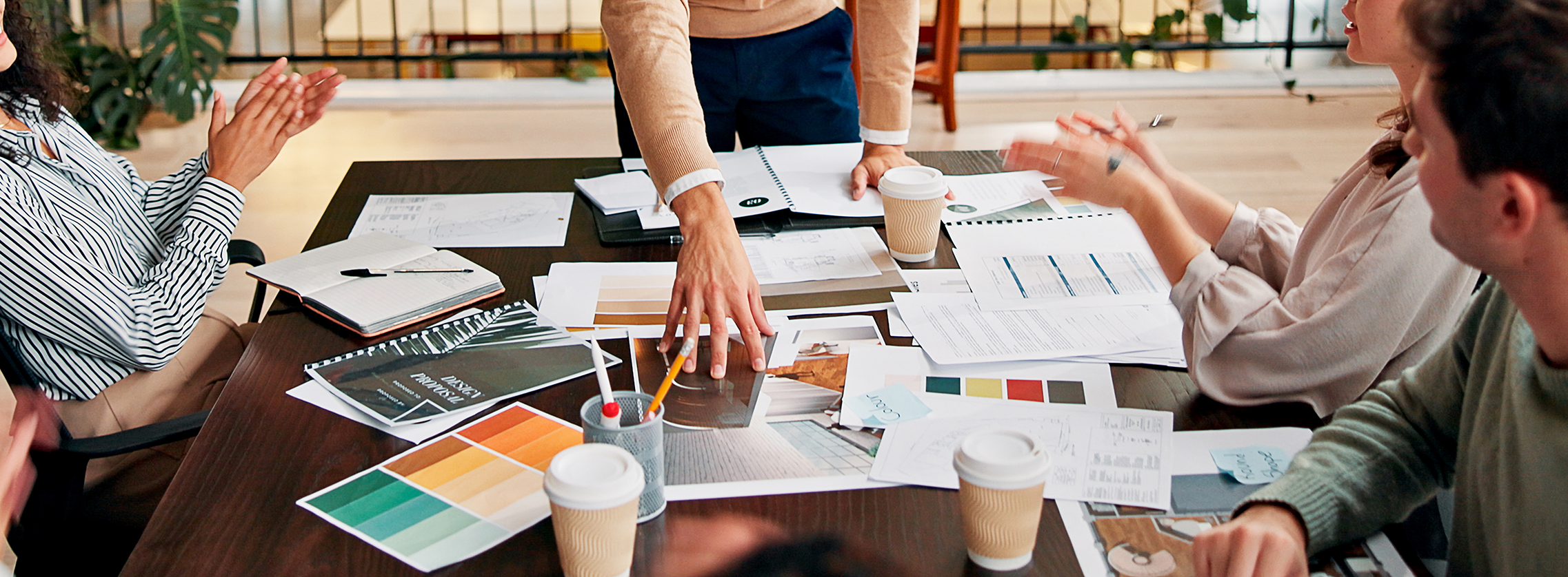 A group of colleagues in a meeting, discussing and deciding all aspects of a brand foundations, with colour palettes, moodboards and other documents on the table.